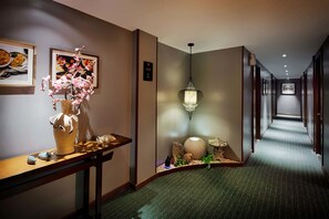 A hotel hallway with a wooden reception desk, a vase with pink flowers, a hanging light fixture, and a carpeted floor. - Silverland Sakyo Hotel & Spa (Ho Chi Minh City)