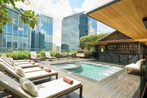 A rooftop pool area with lounge chairs, a bar, and a view of city buildings.