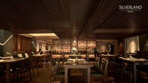 A modern dining area with wooden tables and chairs, a central chandelier, and decorative wall shelves. - Silverland Sakyo Hotel & Spa (Ho Chi Minh City)