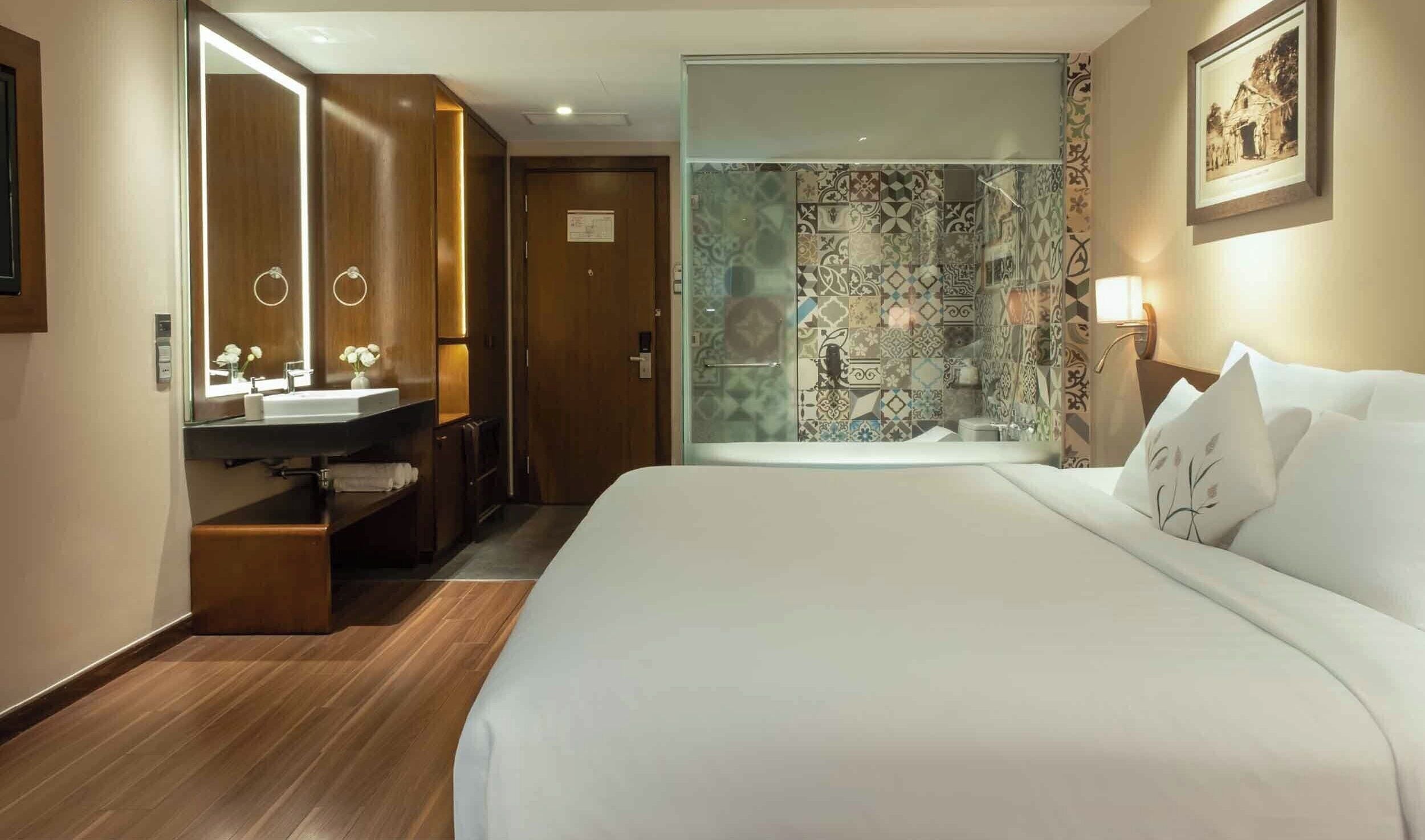 Een hotelkamer met een bed, een badkamer met een douche, een wastafel met spiegel, en een ingelijst schilderij aan de muur.