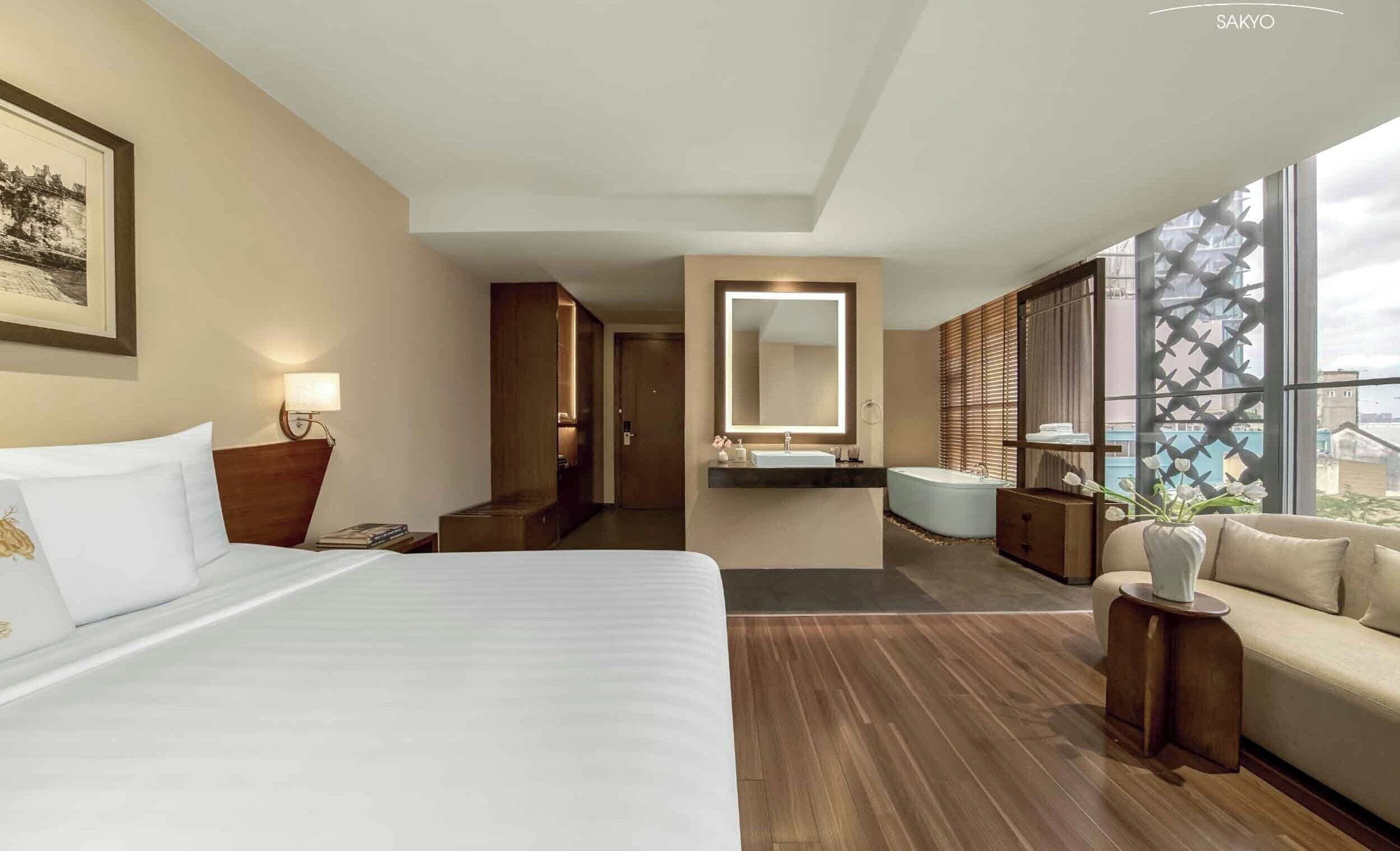 Ein Hotelzimmer mit einem großen Bett, einer Sitzecke, einem Badezimmer mit Badewanne und Blick durch große Fenster.