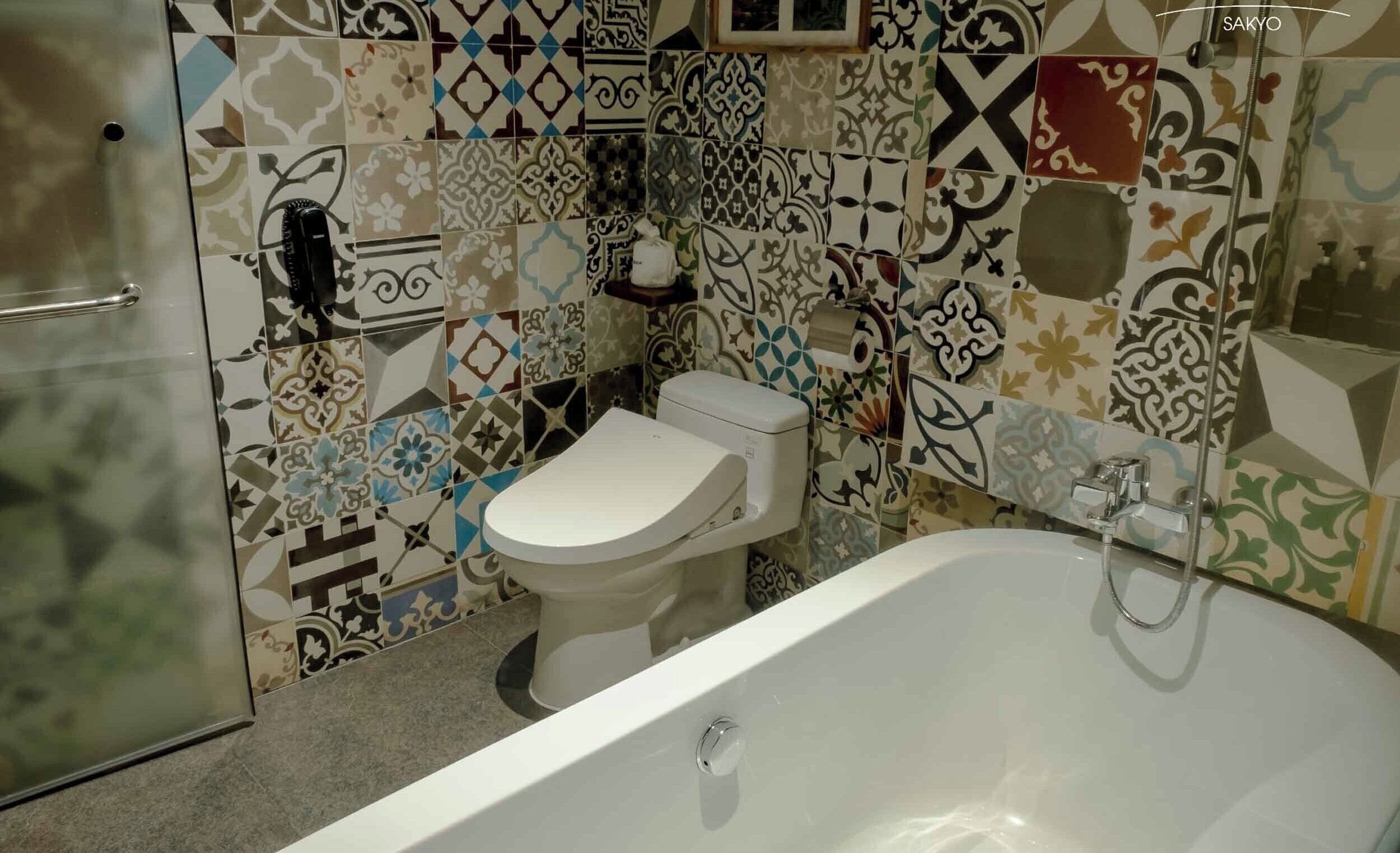 A bathroom with a toilet, a bathtub, and a shower. The walls are tiled with various patterns.