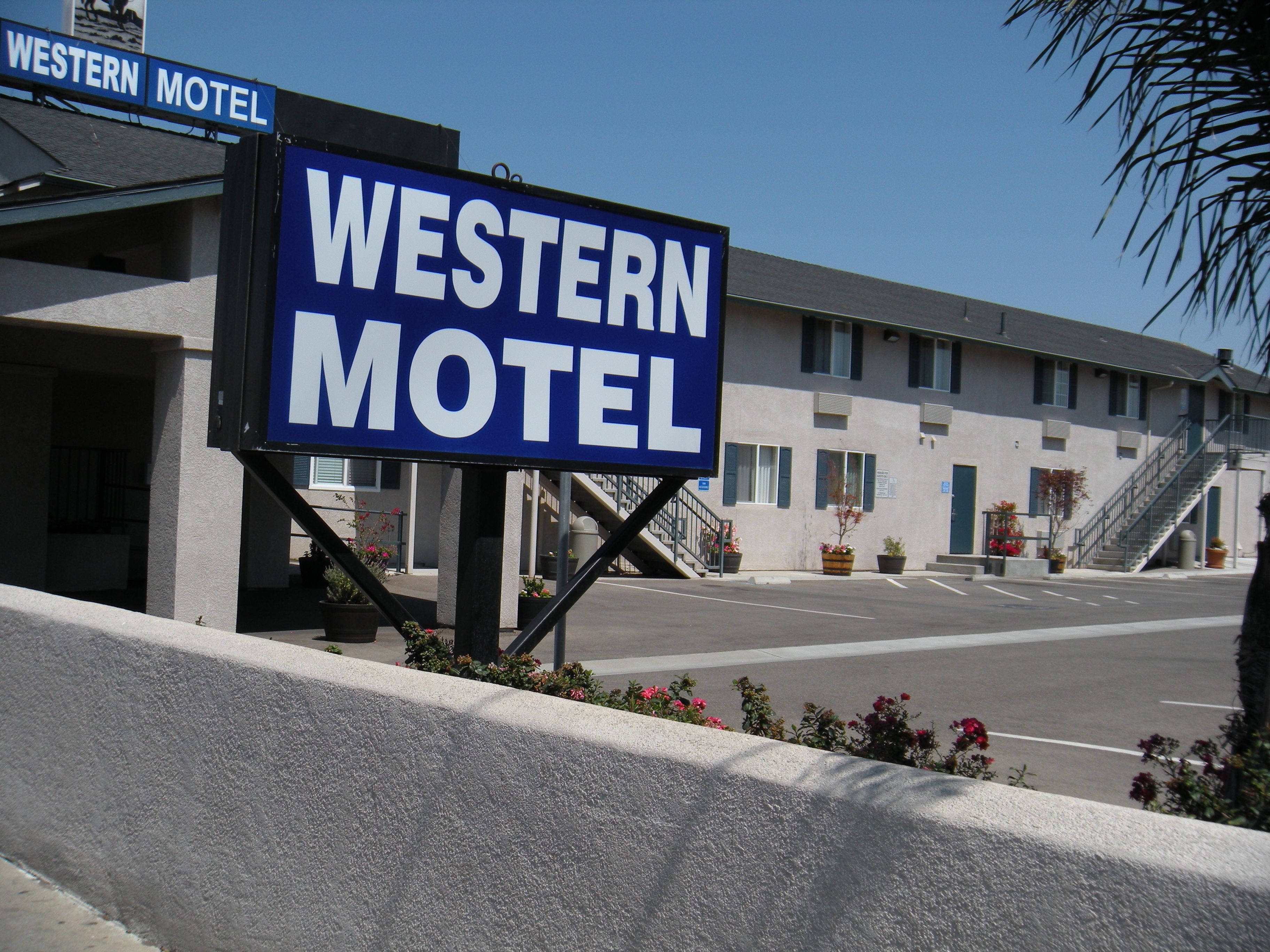 Placa do Western Motel com boa visibilidade da fachada do edifício, incluindo estacionamento e escadas que levam à entrada.
