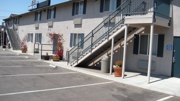 A motel with a staircase leading to the entrance, a parking lot, and potted plants. - Western Motel (Salinas)