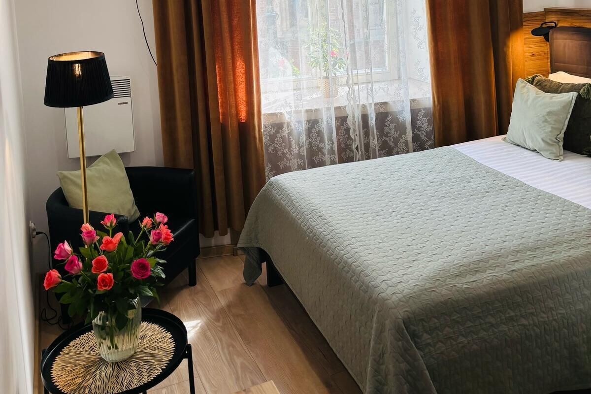 A hotel room with a bed, a flat-screen TV mounted on the wall, a lamp, and a window with curtains.