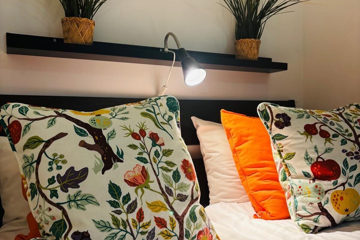 A bed with floral-patterned pillows and a nightstand with a lamp.