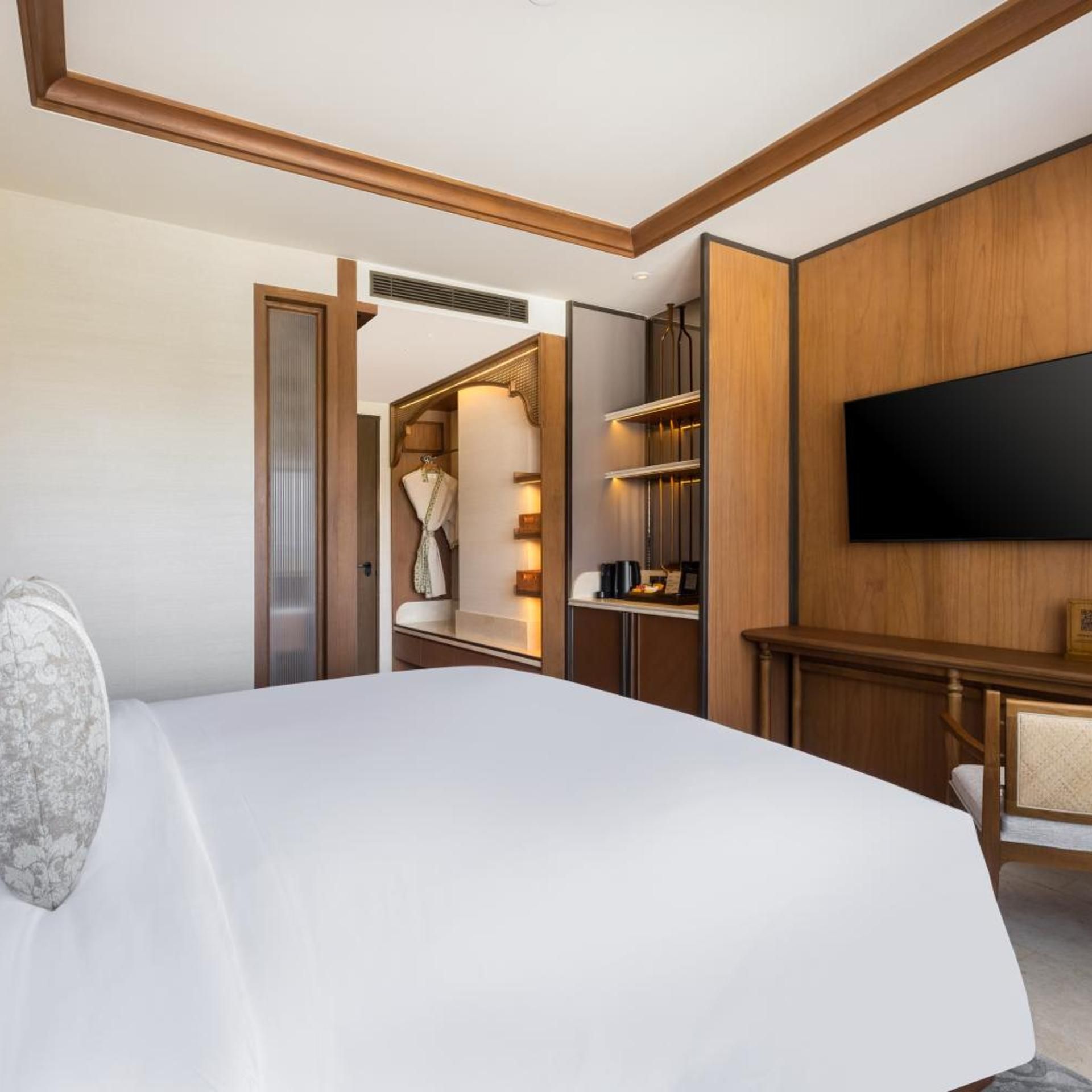 A hotel room with a large bed, a wardrobe, a television mounted on the wall, and a desk with a chair.