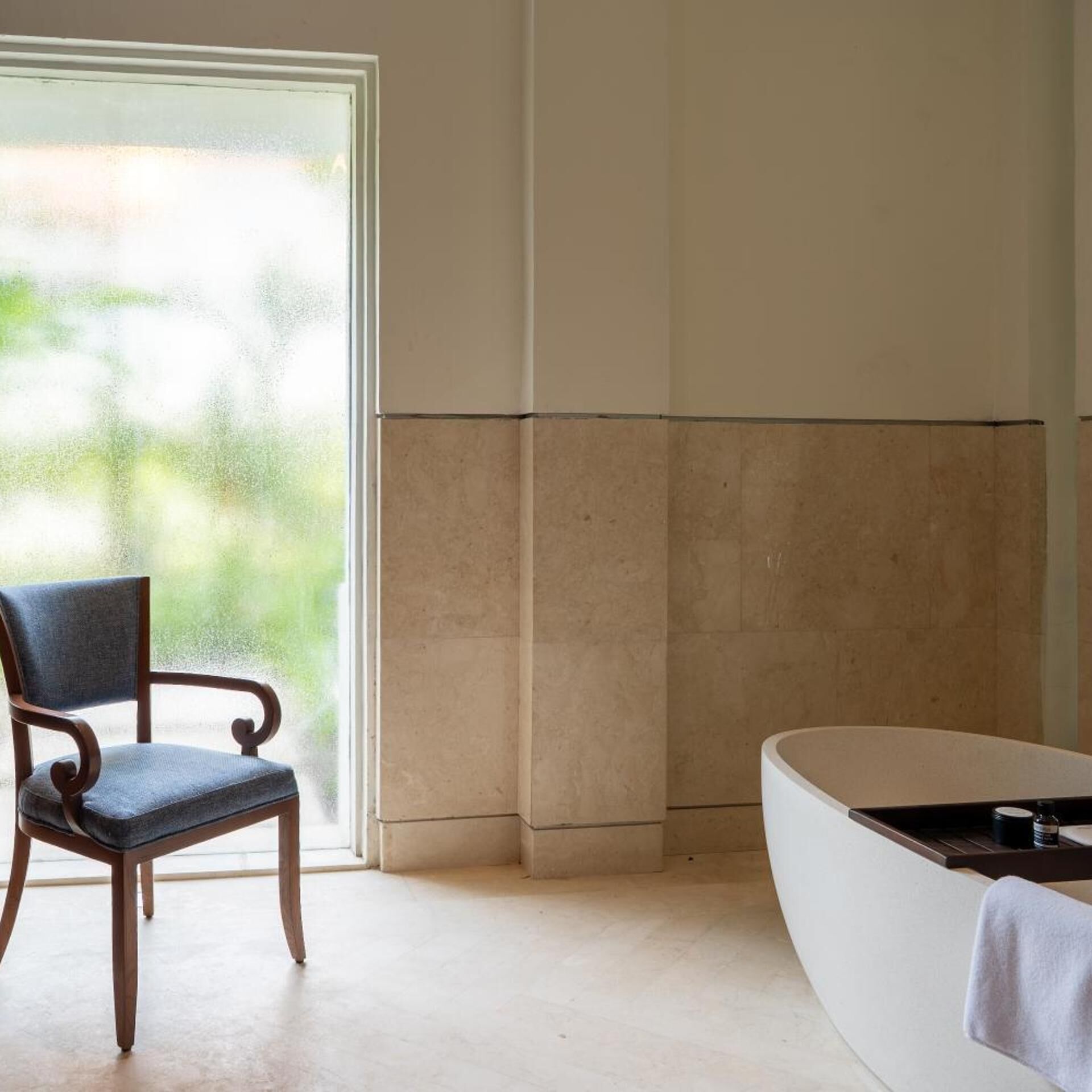 A bathroom with a bathtub, a chair, and a large window.