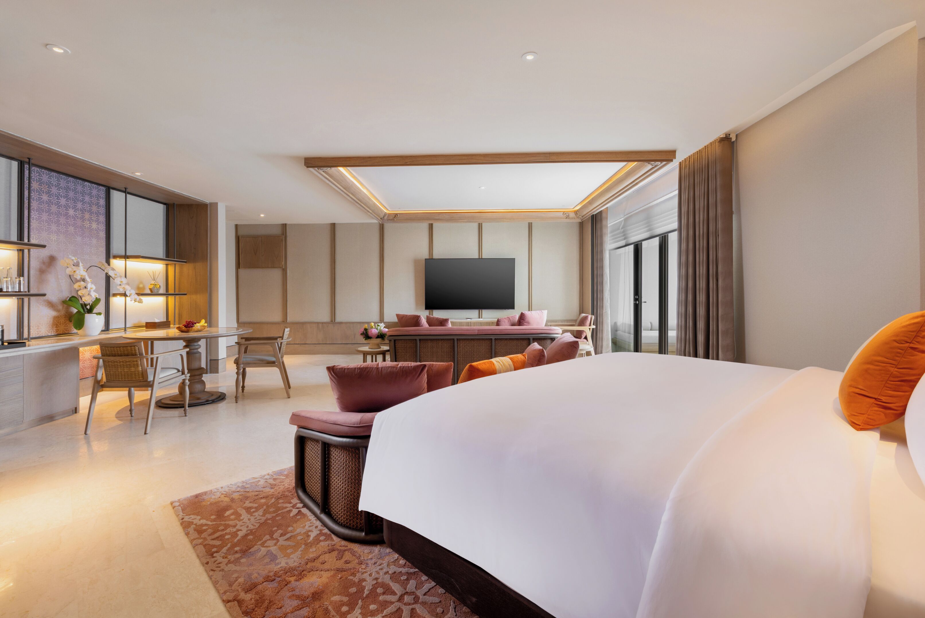 A modern hotel room with a large bed, a dining area, and a TV.