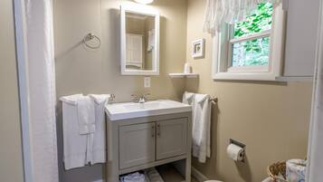 Un baño con lavamanos, espejo, inodoro y ventana con cortinas.