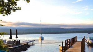 A waterfront deck with lounge chairs, a sailboat, and a dock extending into calm water. - The Juliana Resort (Diamond Point)