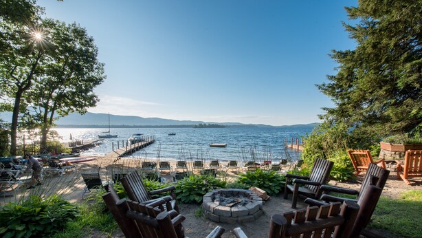 A lakeside patio with wooden chairs, a fire pit, and boats in the background. - The Juliana Resort (Diamond Point)