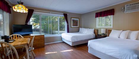 A room with two beds, a desk with a chair, a television, and a window with curtains.