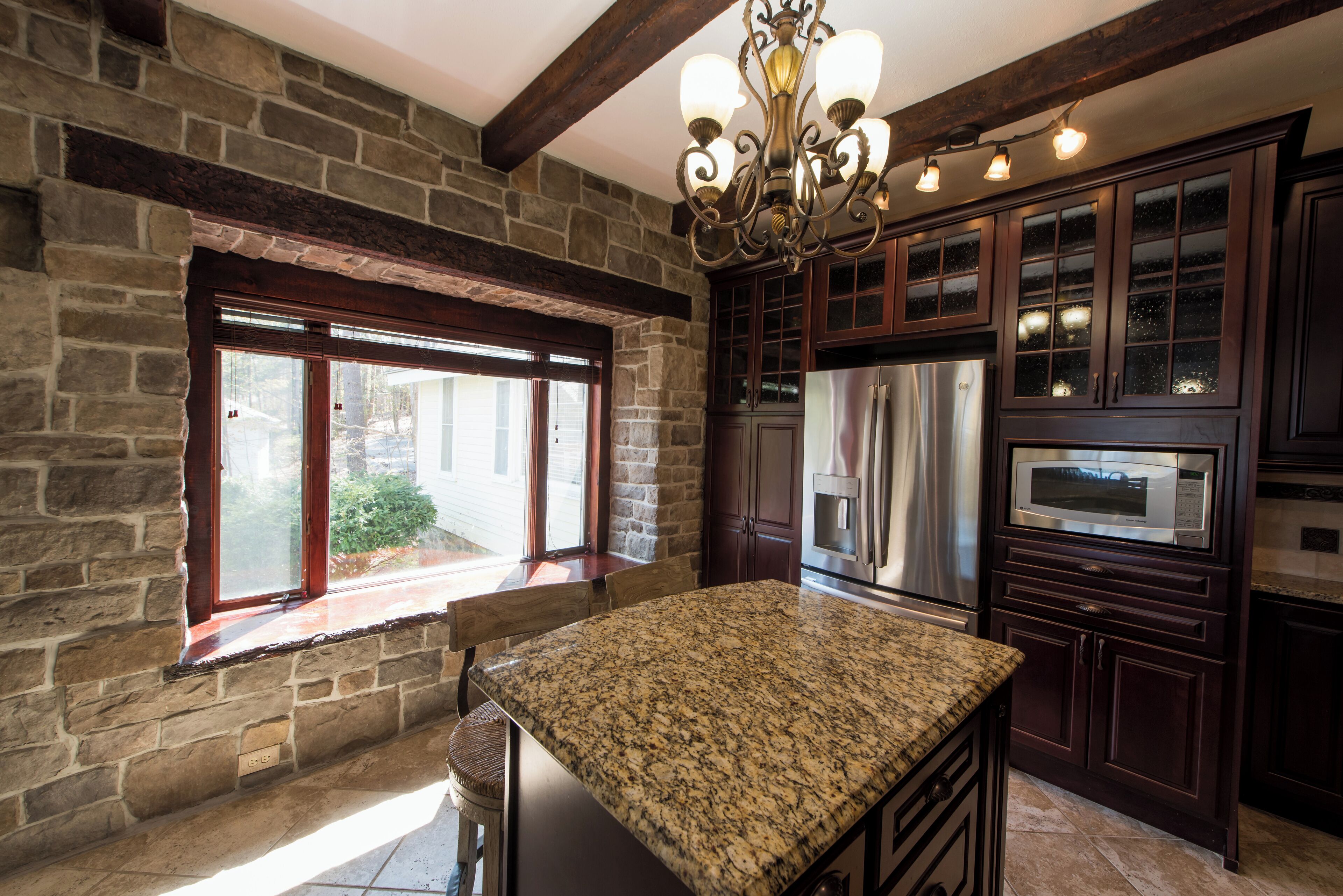 A kitchen with a granite countertop, stone walls, wooden cabinets, and stainless steel appliances.