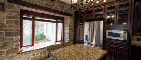 A kitchen with a granite countertop, stone walls, wooden cabinets, and stainless steel appliances.