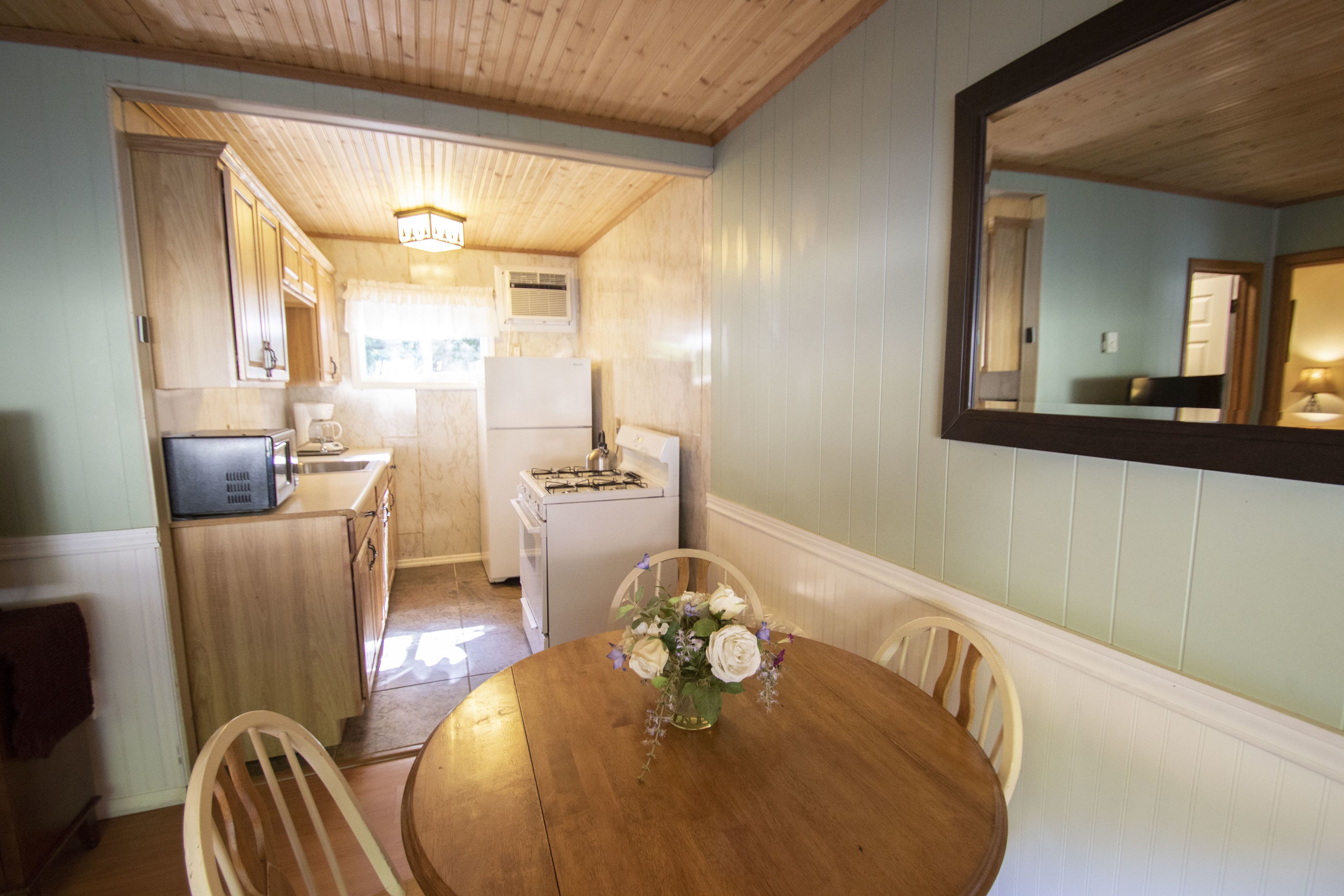 A compact kitchen with wooden cabinets, a refrigerator, and a dining table with chairs.