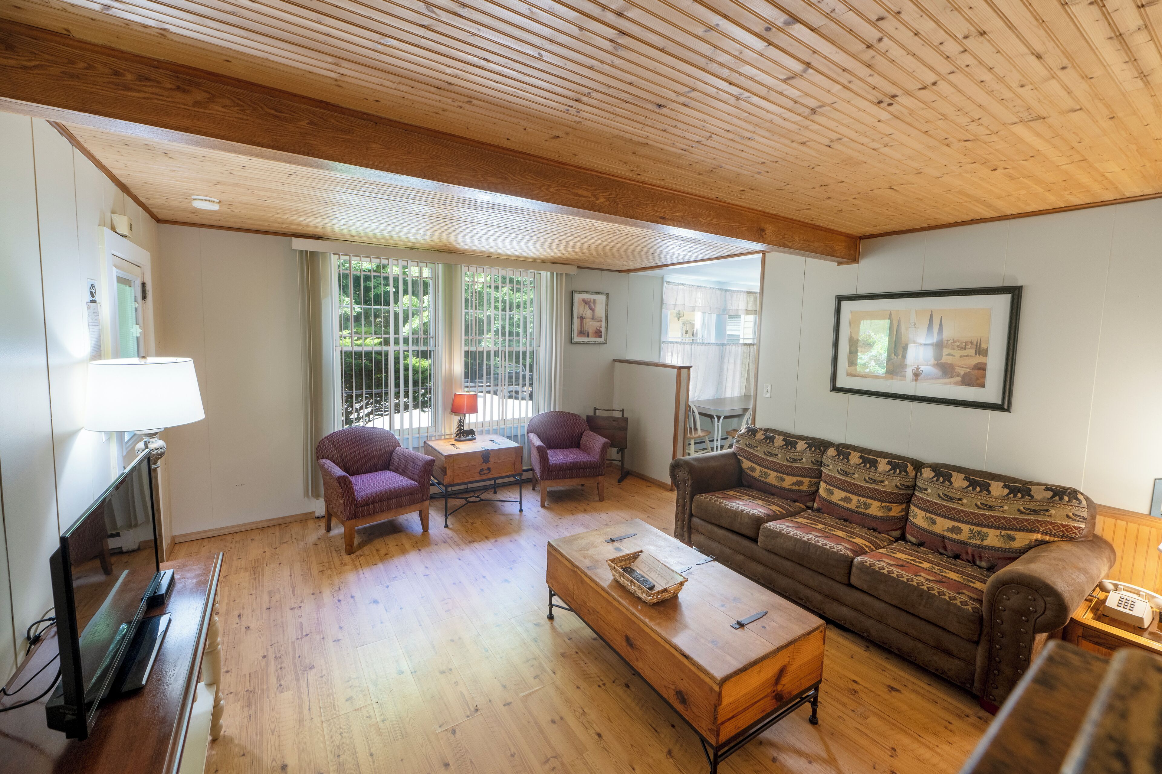 A cozy living room with wooden floors, a sofa, two armchairs, a coffee table, and a TV.