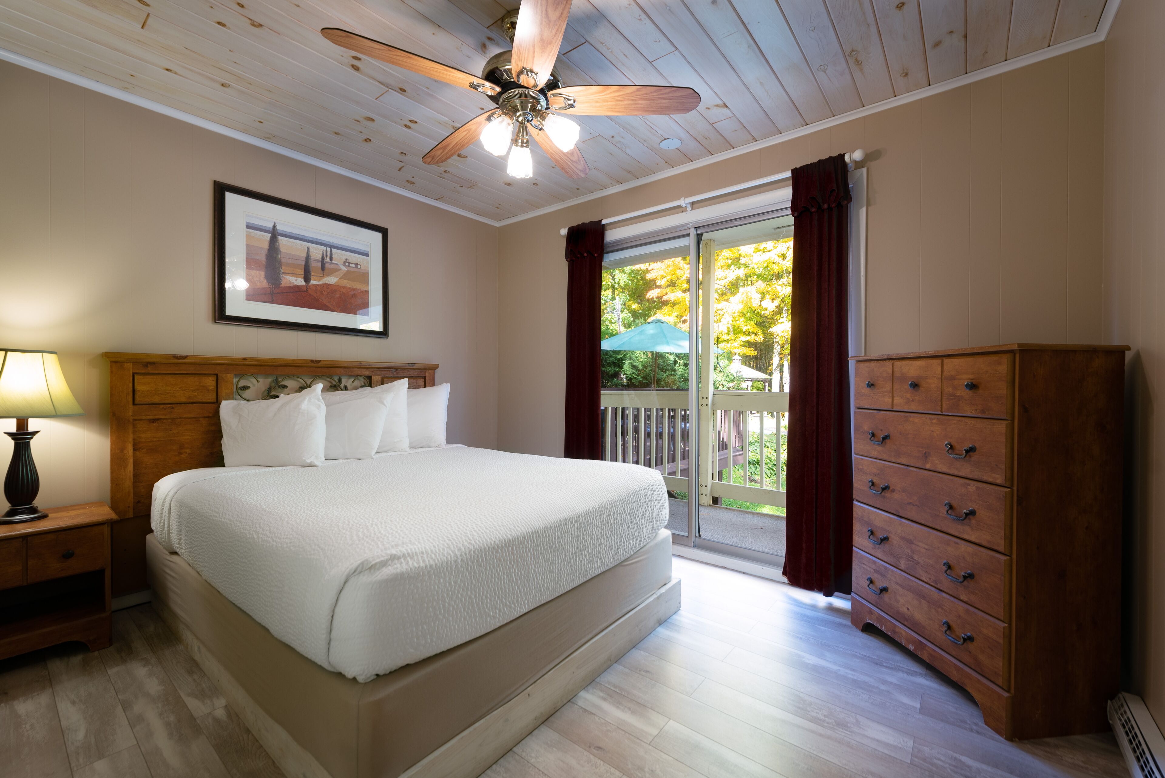 A bedroom with a bed, a ceiling fan, a dresser, and a window with curtains.