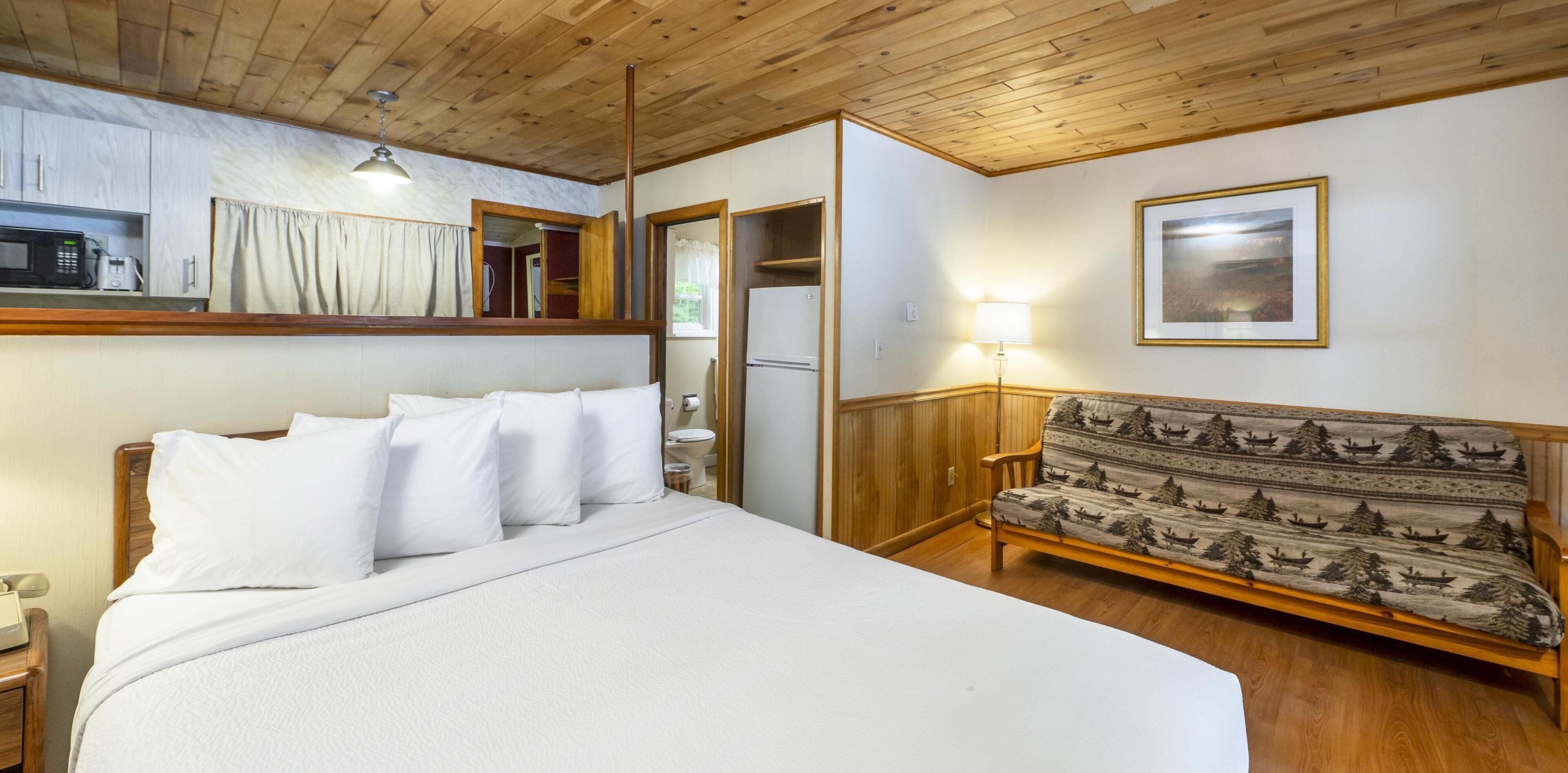 A bedroom with a large bed, a wooden bench, a microwave, and a framed picture on the wall.