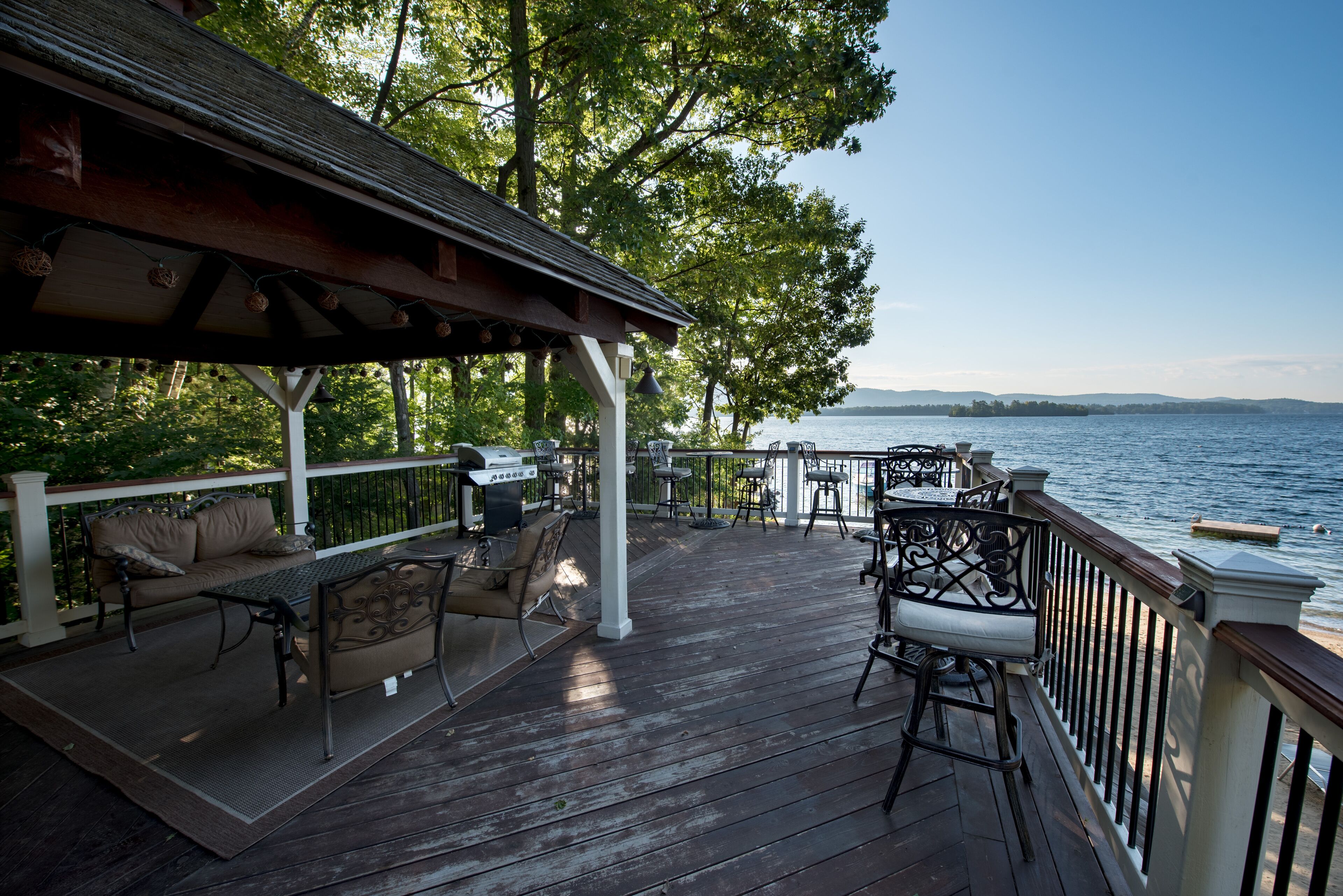 A wooden deck with outdoor furniture, a covered seating area, and a view of a body of water.