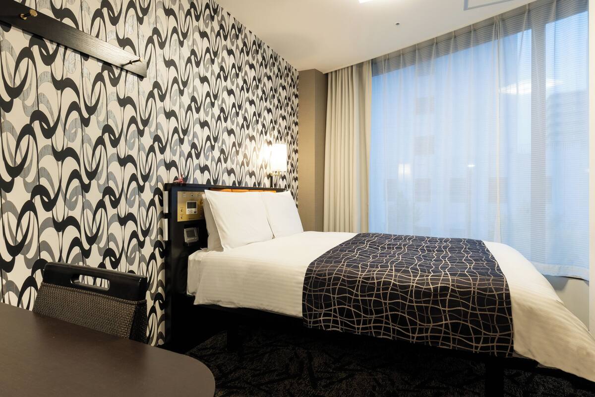 Een hotelkamer met behang met een patroon, een bed met een bedspreider met een patroon, een bureau en een stoel.