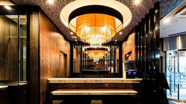 Eine Hotelhalle mit einer prunkvollen Kristallleuchter, Holzvertäfelung, Marmorstufen und einer Rezeption mit digitalem Bildschirm.