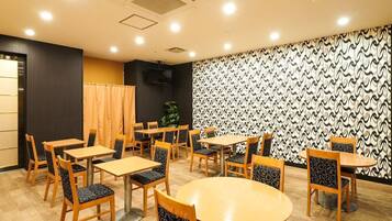 A dining area with multiple tables and chairs, a patterned wall, and a plant.