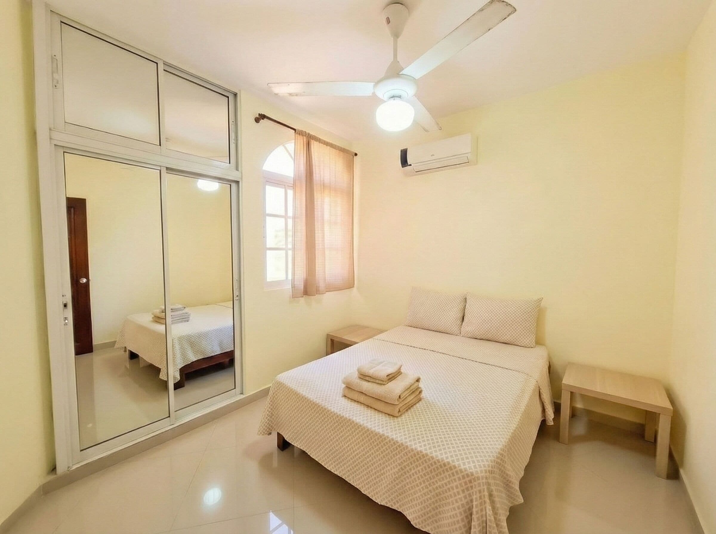 Un dormitorio con cama, mesita de noche y ventilador de techo, además de aire acondicionado.