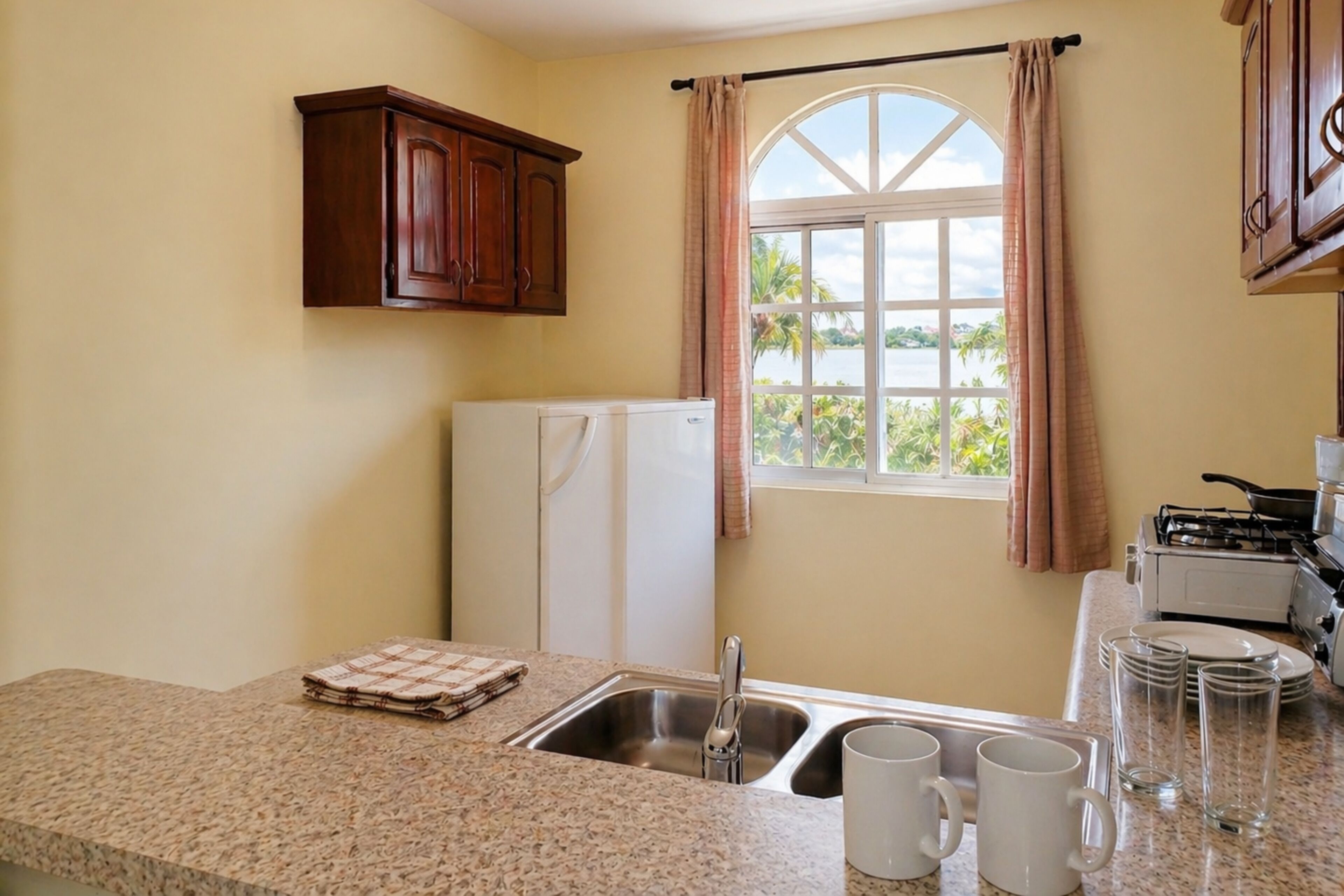 Una cocina con encimeras de granito, un lavamanos, un refrigerador y una ventana con cortinas.
