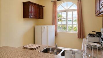 A kitchen with granite countertops, a sink, a refrigerator, and a window with curtains.