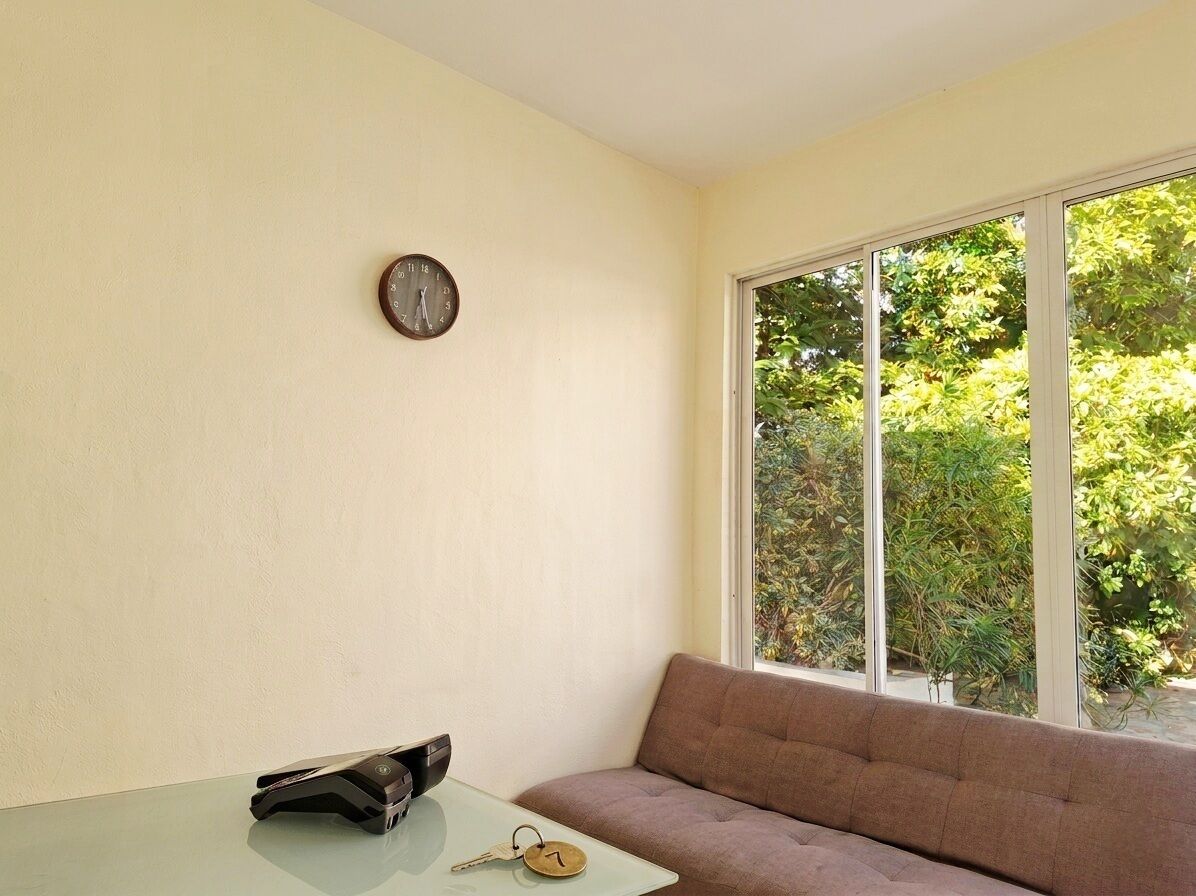 A room with a sofa, a table with keys, a clock on the wall, and a window with a view of greenery.