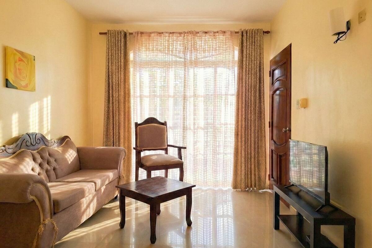 A living room with a sofa, a chair, a coffee table, a television on a stand, and a door.