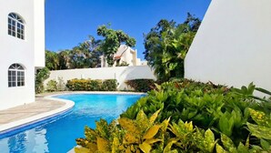 Una piscina circondata da vegetazione rigogliosa e edifici bianchi.