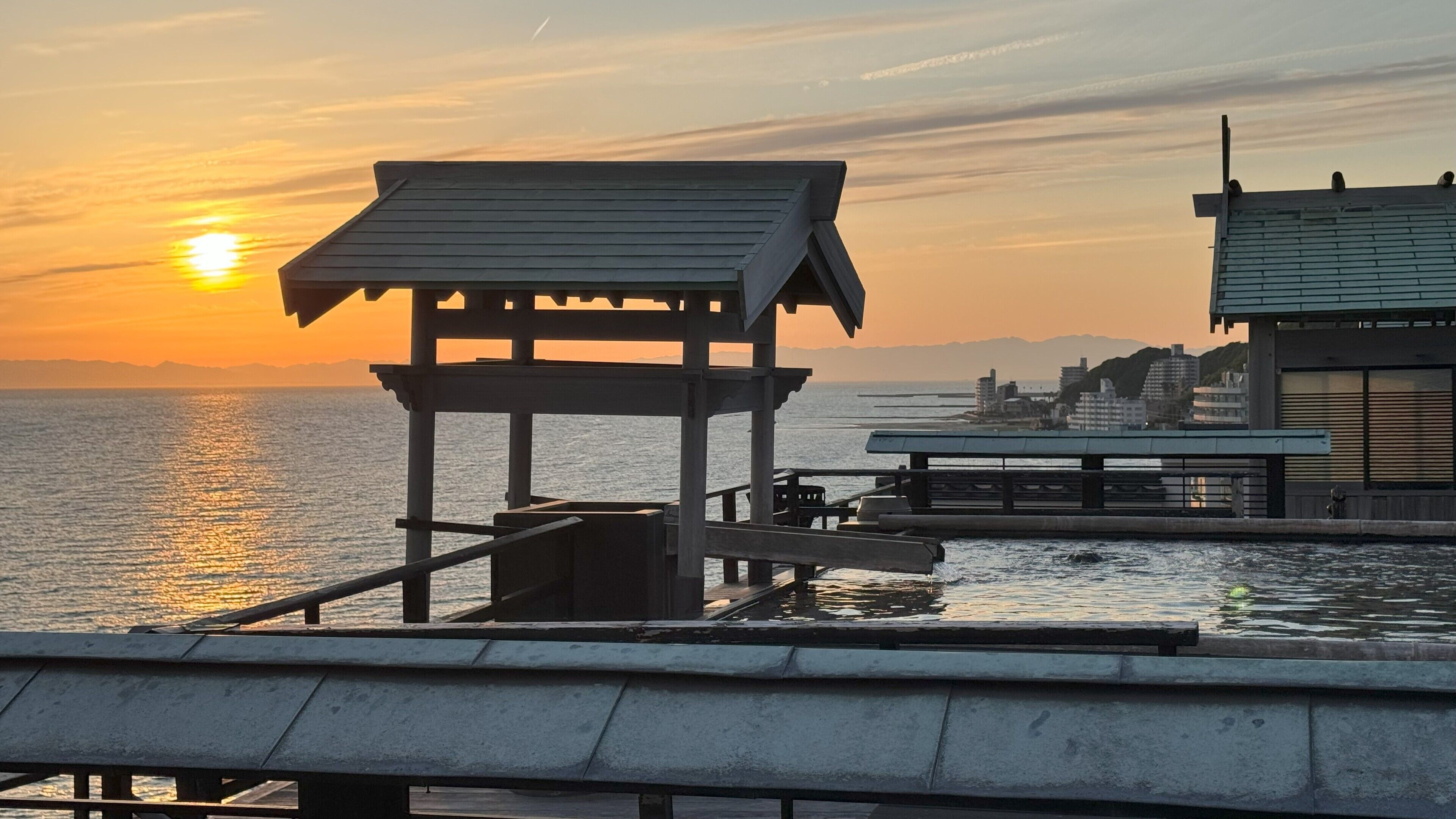 A pier with a wooden structure and a modern building in the background.