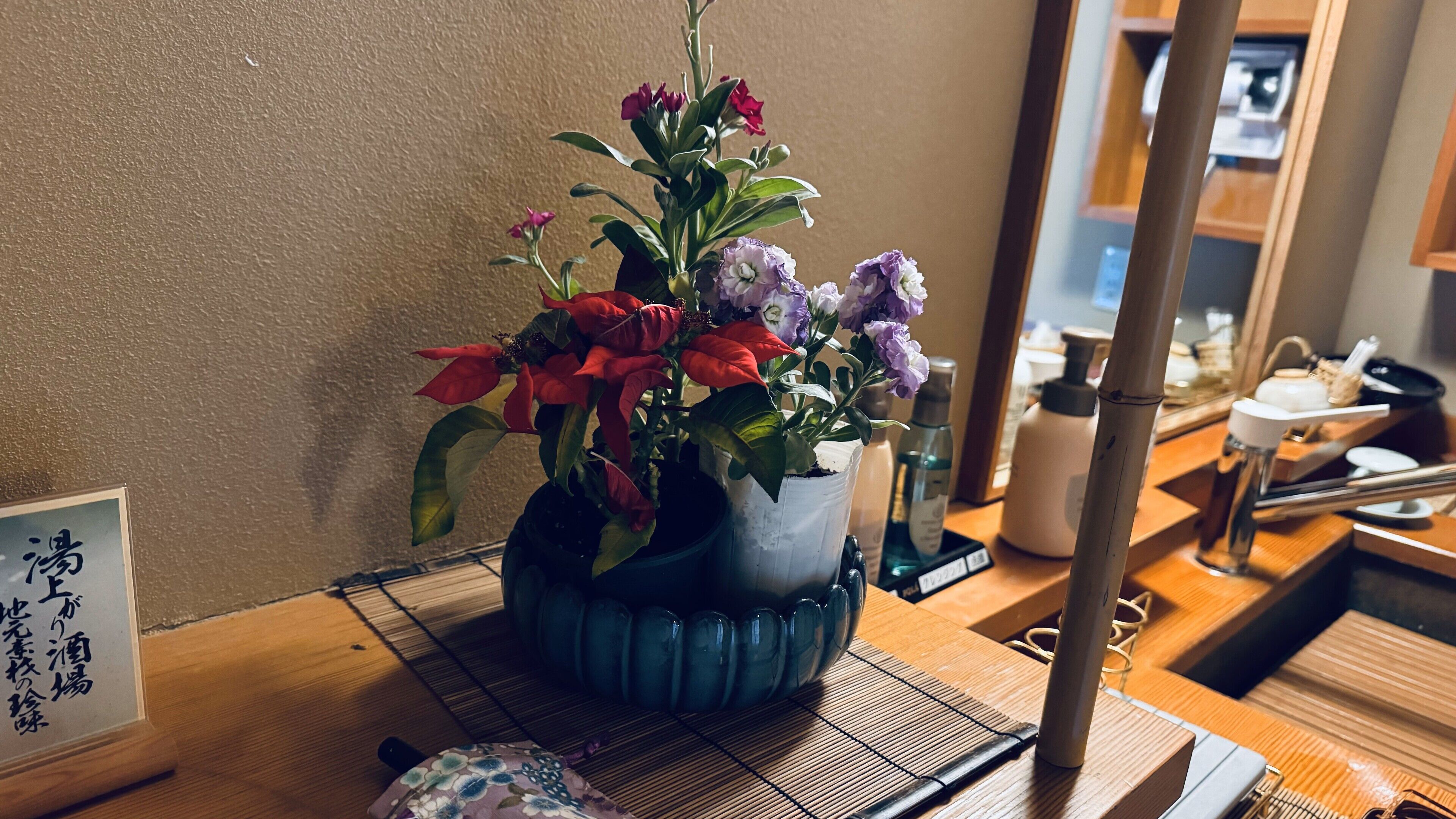 Ein Holztisch mit einer blauen Vase, die eine Blumenkomposition enthält, einer Bambusmatte und einem kleinen dekorativen Gegenstand.