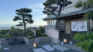 Een traditioneel Japans gebouw met uitzicht op zee, stenen lantaarns en een houten hek.