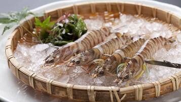 A basket of cooked shrimp on ice with a knife and some greens.