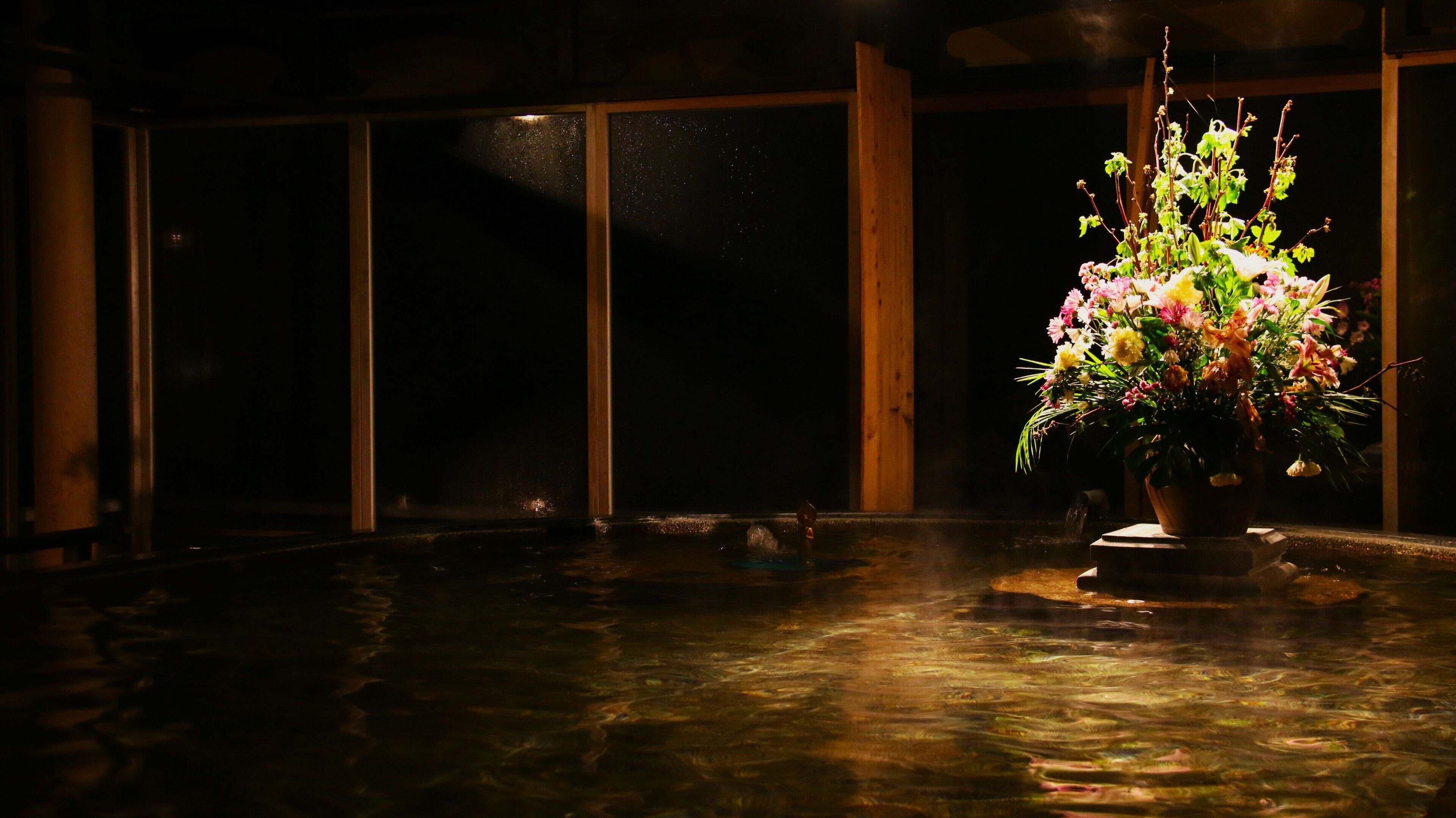 Una habitación con un ventanal grande, una fuente de agua y un arreglo floral.