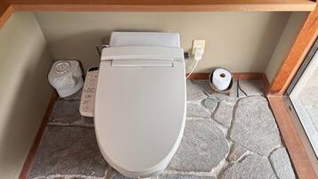 A toilet with a control panel, a toilet paper holder, and a power outlet on the wall.