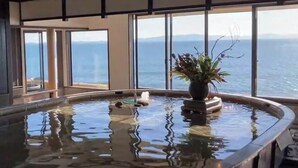 Een wellnessruimte met een jacuzzi, een potplant en uitzicht op de oceaan door grote ramen.