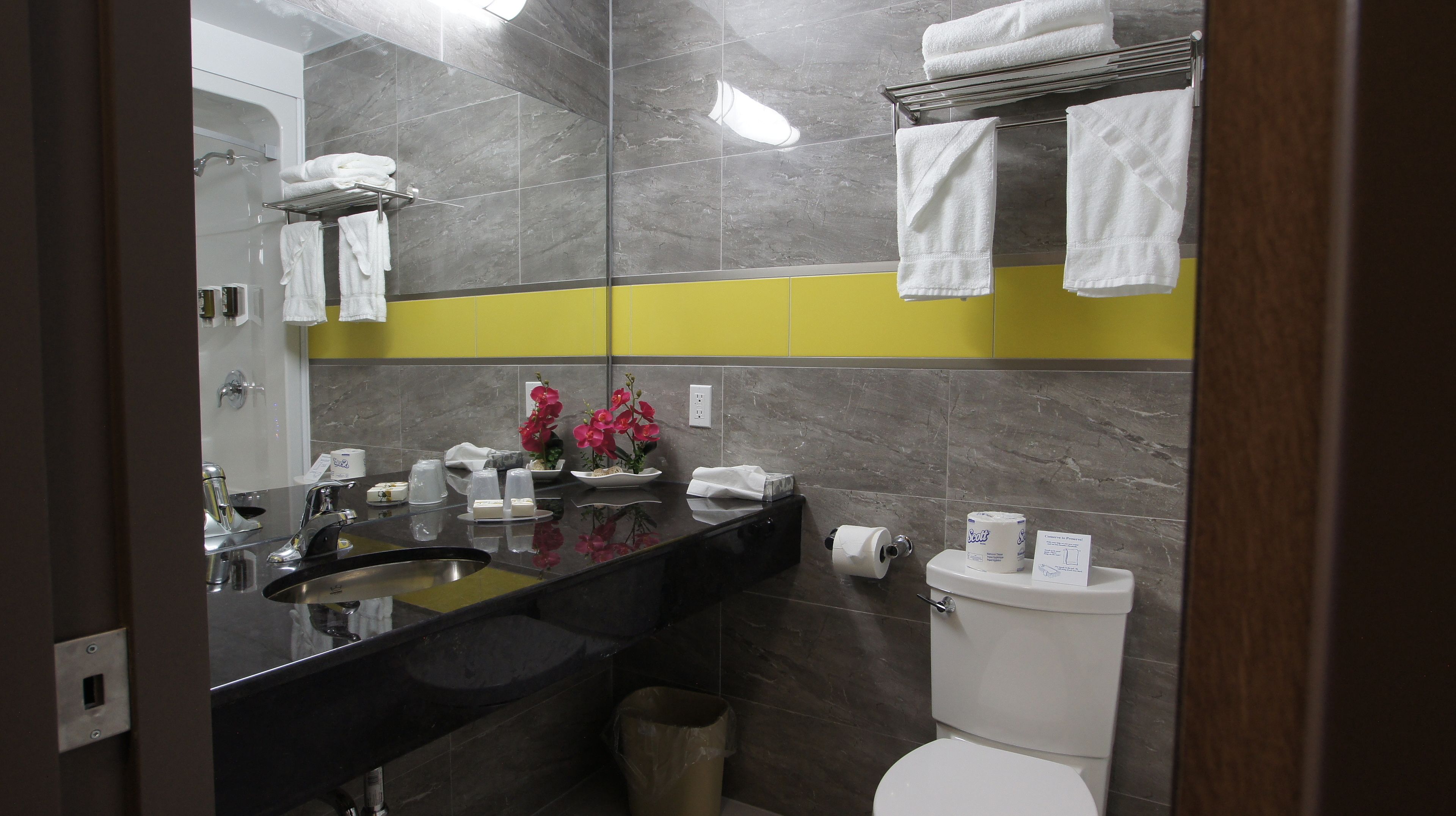 A modern bathroom with a black sink, mirror, and white toilet. There are towels on a rack and a trash can.