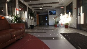 A modern lobby with a leather sofa, potted plants, a staircase, and a TV screen. - Dreamz Inn (Central Huron)