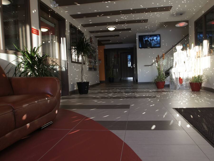 Un hall d’entrée moderne avec un canapé en cuir, des plantes en pot, un escalier et un écran de télévision.