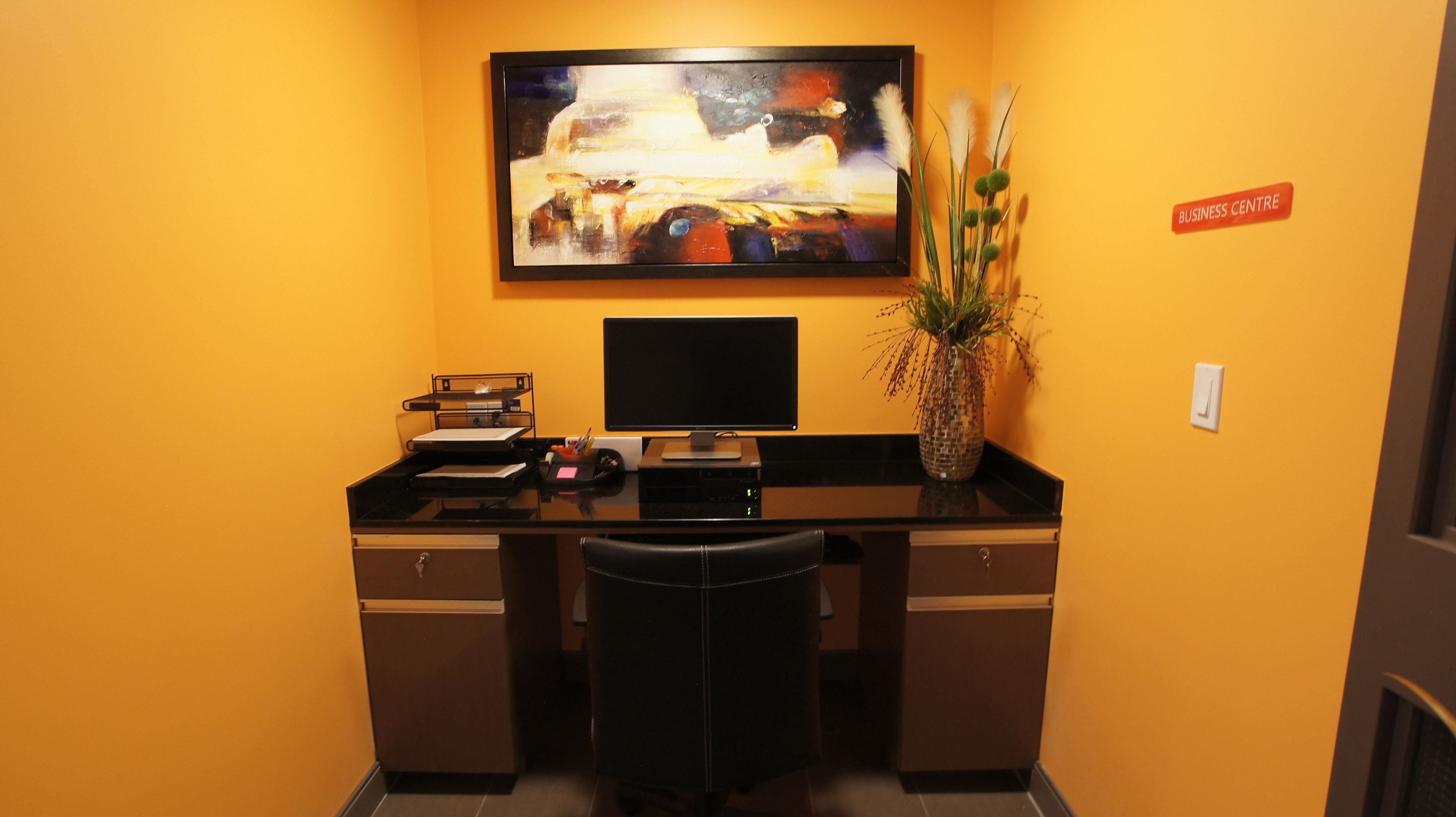Un petit bureau avec un bureau, un ordinateur et un tableau accroché au mur.