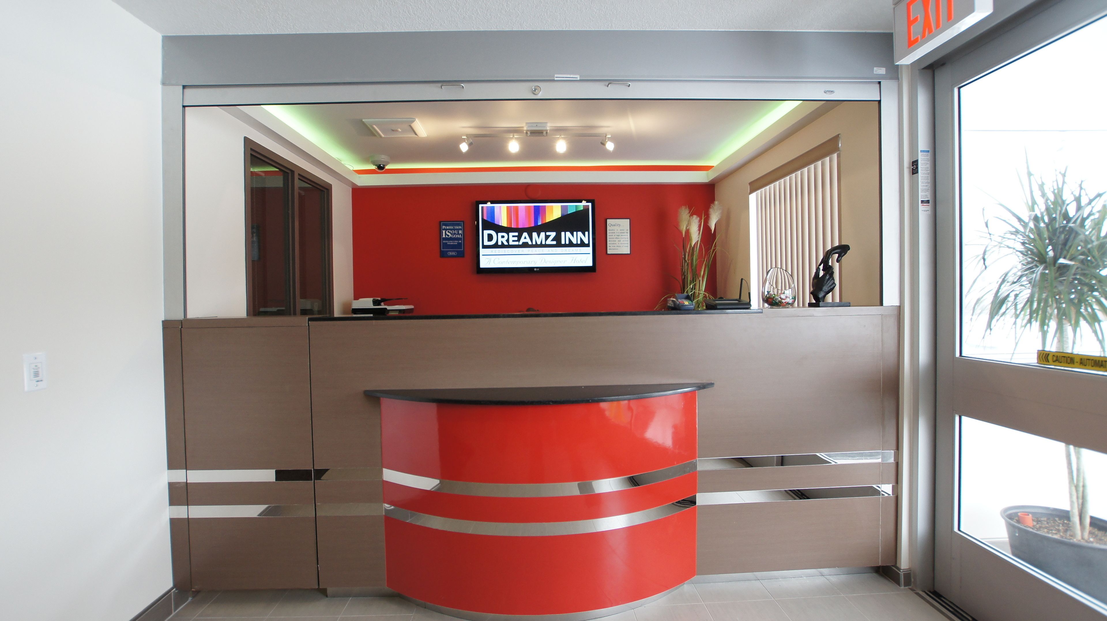 A reception desk with a red and beige color scheme, a mounted television, and a window with a view of a plant.