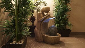 A stone sculpture of a figure holding a light source, surrounded by potted plants and a decorative stone fountain. - Dreamz Inn (Central Huron)