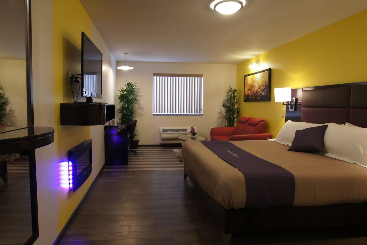 A hotel room with a bed, a desk, a TV, and a window with blinds.