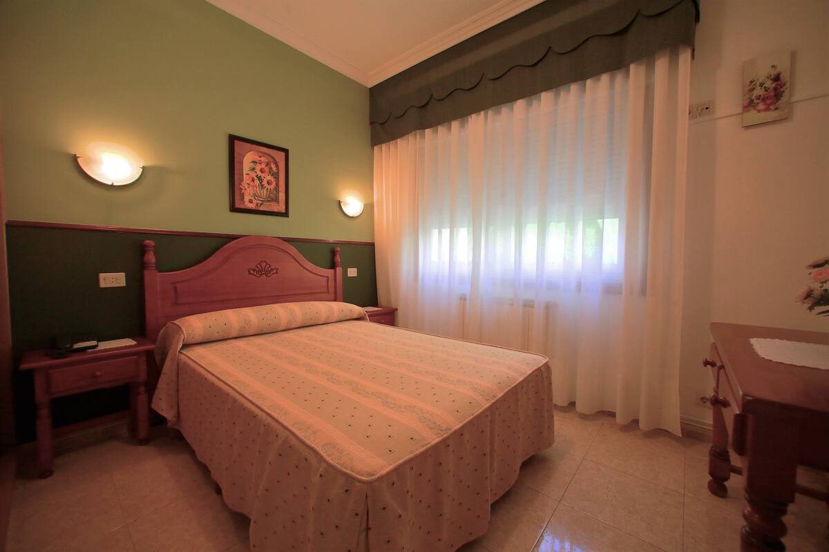 Un dormitorio con cama, mesitas de noche, cómoda, espejo y ventana con cortinas.