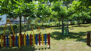 A playground with swings, a slide, and a climbing structure, surrounded by trees and grass. - Hotel La Costera (Sanxenxo)