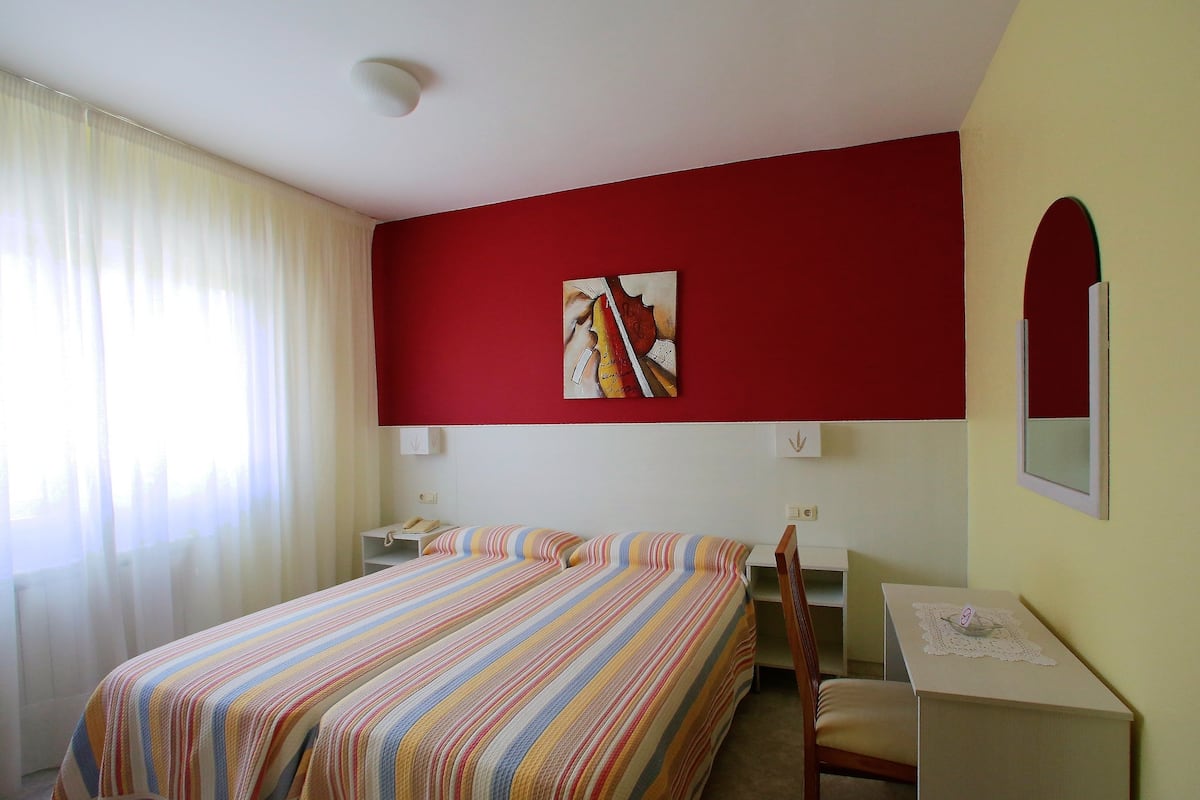 Habitación de hotel con dos camas, un escritorio, una silla, un espejo y un cuadro en la pared.
